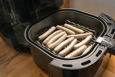 Rohe Schweinew?rstchen, in Deutschland N?rnberger Rostbratwurst genannt, liegen in einer Hei?luftfritteuse auf einem Gestell, um mit wenig ?l gebraten zu werden, ausgew?hlter Schwerpunkt-stock-foto