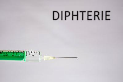 This photo illustration shows a disposable syringe with hypodermic needle, DIPHTERIE written on a white board behind Ger-stock-photo