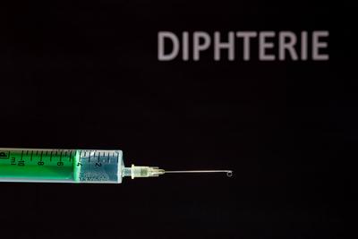This photo illustration shows a disposable syringe with hypodermic needle, DIPHTERIE written on a black board behind Ger-stock-photo