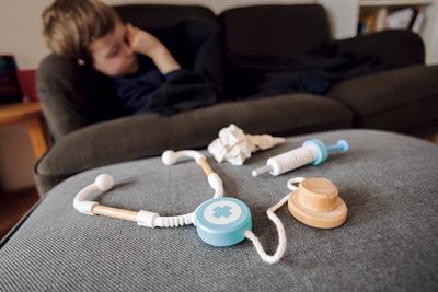 Symbolfoto zum Thema krankes Kind: Ein fuenfjaehriger Junge liegt zu Hause auf einer Couch hinter einem Stethoskop, eine-stock-foto