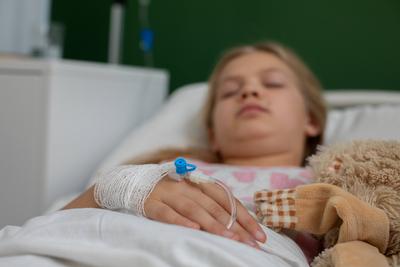 Ein Kind in einem Krankenhausbett mit einer Infusion h?lt ein Stofftier als Symbol der Hoffnung w?hrend der Genesung-stock-foto