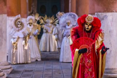 A group of masked persons in creative white and red costumes, posing between big pillars, celebrating the Venetian Carni-stock-photo