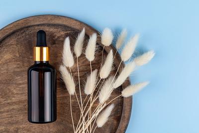 Blank Bernstein Glas ?therisches ?l Flasche mit Pipette auf runden Holztablett auf blauem Hintergrund dekoriert lagurus Bouquet. Hautpflegekonzept mit Naturkosmetik-stock-photo