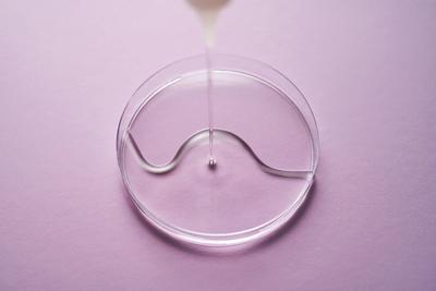 Serum or cosmetic oil flows into a transparent bowl on a purple background. Serum or cosmetic oil flows into a transpare-stock-foto