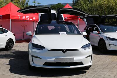 Tesla Model X (Modelljahr 2023, Farbe: Pearl White Multi-Coat / Weiss) mit ge?ffneten Fl?gelt?ren vor Tesla - Schriftzug-stock-foto