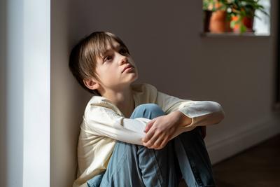 Einsamer Junge schaut traurig auf und umarmt seine Knie, w?hrend er allein zu Hause am Fenster sitzt. Kind psychologisches Trauma-stock-foto