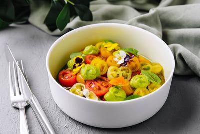 Frischer Tomatensalat mit essbaren Bl?ten Vibrant salad of cherry tomatoes and gooseberries garnished with edible flower-stock-foto