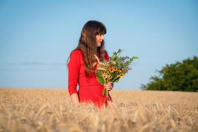 H?bsche Frau mit einem Blumenstrau? in der Hand steht erfreut in einem reifen Getreidefeld. Junge und attraktive Frau mi-stock-photo