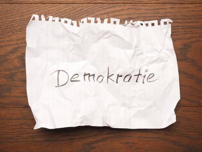 Wrinkled paper with the German word democracy on a wooden table-stock-photo