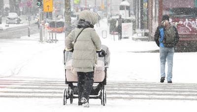 Wintereinbruch in Hamburg. Eine Frau geht bei dichtem Schneefall mit einem Kinderwagen auf einem Gehweg entlang. Winterh-stock-foto