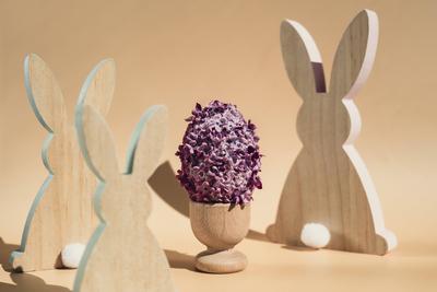 Wooden minimalism low-key bunny decor. Easter egg made of lilac spring flowers in pastel beige background. Sustainable holiday minimalistic still life composition. Copy space template for invitation greeting card-stock-photo