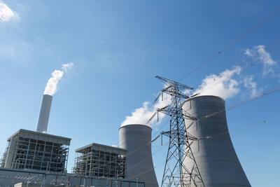 thermal power plant and electricity pylon modern thermal power plant and high voltage transmission pylon against a blue-stock-foto