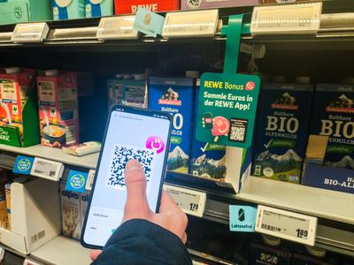 Bavaria, Germany - January 21, 2025: A customer holds his smartphone with the REWE Bonus app open in front of an adverti-stock-foto