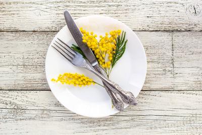 Festive table setting plate with fork and knife and mimosa flower decoration on white wooden background with copy space-stock-foto