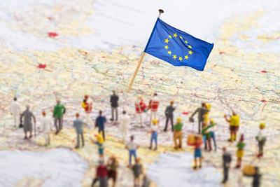 Symbolfoto Fl?chtlinge mit Ziel Europa Europakarte mit Europ?ischer Flagge und einer gro?en Gruppe mit Figuren. Copyrigh-stock-photo