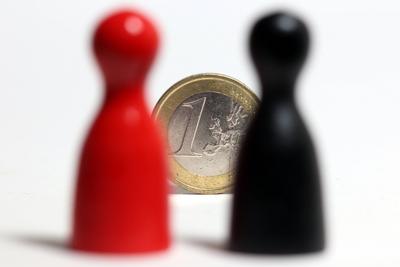 Spielfiguren Mensch aergere dich nicht in den Farben schwarz und rot stehen hinter einer Euro Geldmuenze-stock-foto
