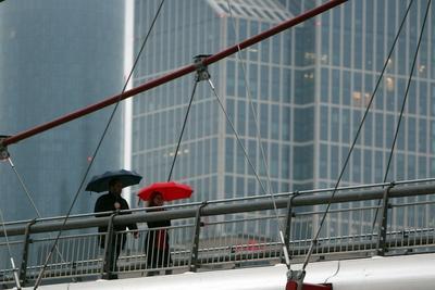 Dauerregen in Frankfurt am Main: Passanten mit Regenschirmen ?berqueren den Holbeinsteg ?ber den Main vor der Skyline d-stock-foto