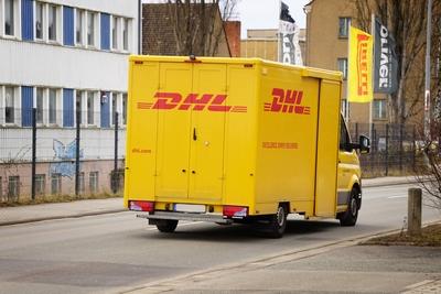 gelber DHL Lieferwagen mit Logo f?hrt auf einer Stra?e, Paketverteilung, Paketdienst, Sendungsverfolgung, Kundenservice-stock-foto