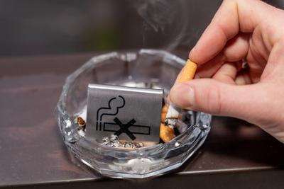 Bavaria, Germany - January 6, 2024: Smoke-free concept, a man puts out a burning cigarette in an ashtray with a no smoki-stock-photo