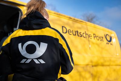 Eine Postbotin tr?gt vor einem Zustellfahrzeug eine Jacke mit dem Logo der Deutschen Post. Rottweil Baden-W?rttemberg De-stock-foto