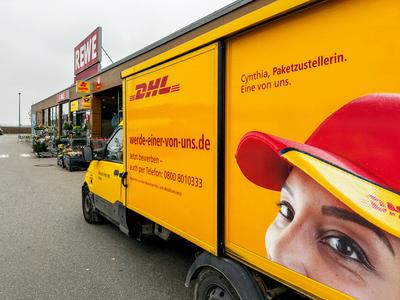 Bavaria, Germany - November 13, 2024: DHL Deutsche Post delivery vehicle with employee advertising in front of a REWE st-stock-foto