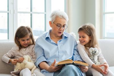 Gl?ckliche Familie zu Hause. Zwei M?dchen Schwestern Zwillinge Gro?mutter lesen Geschichte Buch zusammen. Gute Zeit zu Hause. Oma unterrichtet Enkelinnen lesen Buch M?rchen erz?hlen Geschichte Familie Generationen.-stock-photo
