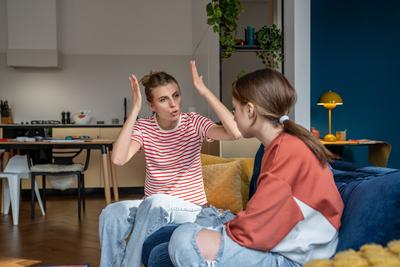 Ver?rgerte Mutter gestikuliert schreiend zu ihrer Teenager-Tochter, die zu Hause auf der Couch sitzt.-stock-photo