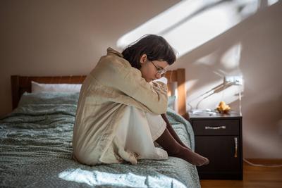 Apathetisches Teenager-M?dchen, das auf dem Bett sitzt und die Knie umarmt, mit dem Gef?hl von Prokrastination, Depression und Einsamkeit-stock-foto