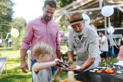 Father, grandfather and son grilling together at garden BBQ. Three generations of men at summer family garden party. Fat-stock-foto