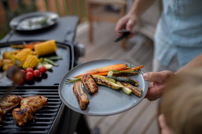 Father putting grilled meat and vegetable on plate to his son during family summer garden party. A father putting grille-stock-foto