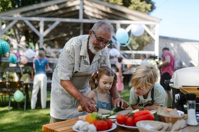 Grandfather teaching kids to cut vegetables for grilling. Grilling together at garden BBQ. Grandchildren with grandfateh-stock-foto