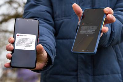 Langweid, Bavaria, Germany - March 13, 2025: Nationwide test alarm in Bavaria. A man holds two smartphones with an EXTRE-stock-foto