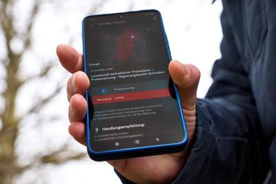 Langweid, Bavaria, Germany - March 13, 2025: Nationwide test alarm in Bavaria. A man holds a smartphone with a warning m-stock-foto