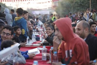 Palestinians break their fast at a table set amidst the destruction and debris caused by Israeli attacks during a mass iftar program in Nusairat in central of Gaza Strip-stock-foto