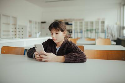 Young schoolgirl sitting in a science lab with a phone in her hand, waiting for classmates.-stock-foto