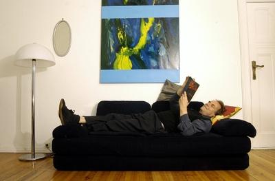 Schriftsteller Peter Schneider (GER) liest auf einem Sofa liegend in seinem Buch in seiner Wohnung in Berlin-stock-foto