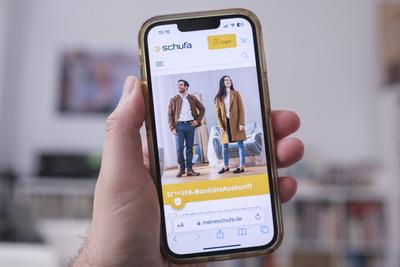 Mobiltelefon in einer Hand mit der Website der Schufa *** Mobile phone in one hand with the Schufa website Nordrhein-Wes-stock-foto