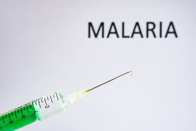 This photo illustration shows a disposable syringe with hypodermic needle, MALARIA written on a white board behind Germa-stock-photo
