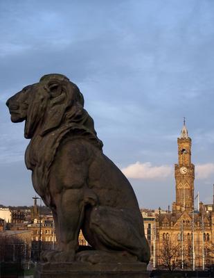 a lion sculpture in profile on the war memorial in Bradford city center with a view of the town hall and buildings form-stock-photo