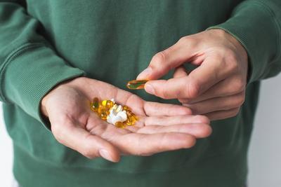 Close-up of hands holding various pills and capsules, illustrating the concept of health, supplements, or medication use, with a green sweater in the background-stock-photo