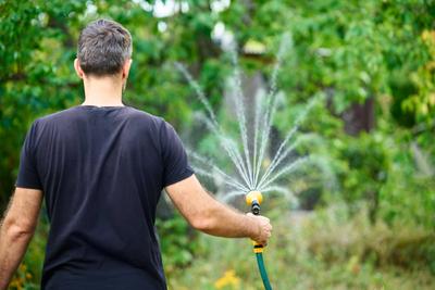 Young man watering flowers and plants in garden with hose Young man watering flowers and plants in garden with hose in s-stock-foto