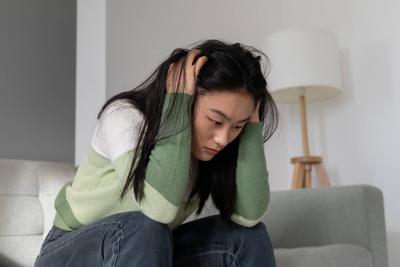 ?ngstliches, besorgtes asiatisches Millennial-M?dchen, das den Kopf in den H?nden h?lt und mit Depressionen nach einer Abtreibung zu k?mpfen hat-stock-foto