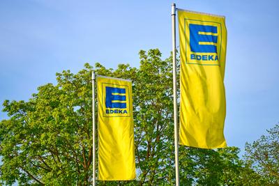 Augsburg, Bavaria, Germany - April 13, 2024: Flag of the German supermarket and food retailer EDEKA in front of green tr-stock-foto