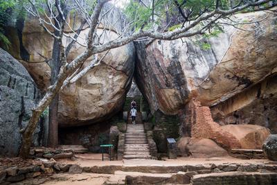 Tourists walking on stairs between two huge stones in Sigiriya, Sri Lanka Sigiriya, Sri Lanka - 23 March 2017: Tourists-stock-photo