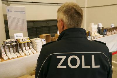 Beamter mit der Aufschrift Zoll auf seiner Jacke bewacht Viagra, Testosteron, Aufputschmittel Medikamente Verpackungen Gold und Geld liegen auf einem Tisch waehrend der Zoll Praesentation von sichergestellten Dopingmitteln, Drogen und Vermoegenswerten wie Bargeld und Gold in einer Halle auf dem Gelaende des Zollfahndungsamtes Hamburg17.04.2025 Der Hamburger Zoll hat einen illegalen Dopingmittel und Drogenvertrieb zerschlagen Die Beamten hatten einen Haendlerring von 3 Bruedern festgenommen die Sachen sichergestellt.Dabei wurden Verm?genswerte in H?he von 189.000 Euro in Bar sowie Gold im Wert von 50.000 Euro Hamburg Deutschland *** Officer with the inscription customs on his jacket guards Viagra, testosterone, stimulant drugs packaging go-stock-foto