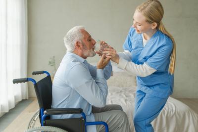 Hilfe zur Unterst?tzung des Wasserhaushalts im Gesundheitswesen. Krankenschwester gibt Glas Wasser f?r alten Mann Patienten im Rollstuhl. Gel?hmter Mann in Stuhl f?r Menschen mit Behinderung trinken frisches Wasser. ?lterer Mann und Krankenschwester zu Ha-stock-photo