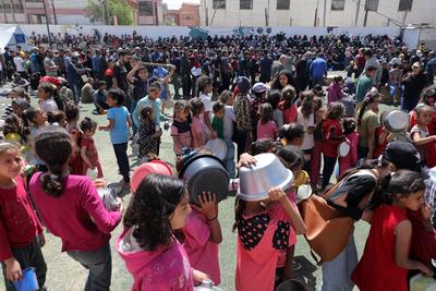 Palestinians, mostly children, wait in long lines with empty pots in hands to get a warm meal distributed by charitable-stock-foto