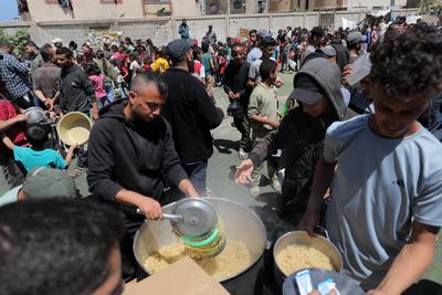 Palestinians, mostly children, wait in long lines with empty pots in hands to get a warm meal distributed by charitable-stock-foto