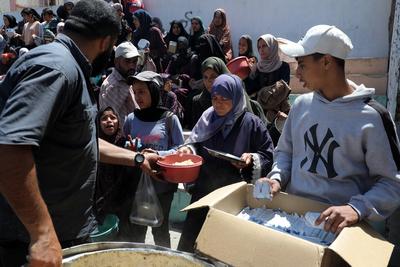 Palestinians, mostly children, wait in long lines with empty pots in hands to get a warm meal distributed by charitable-stock-foto