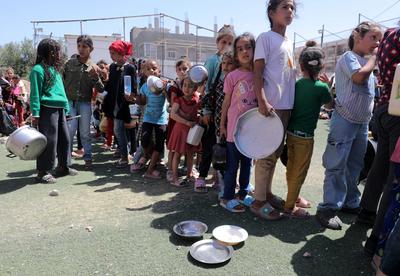 Palestinians, mostly children, wait in long lines with empty pots in hands to get a warm meal distributed by charitable-stock-foto